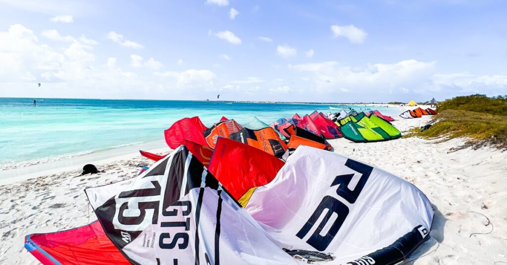 Colorful kitesurfing gear lined up on Venezuela's tropical beach under a bright blue sky.